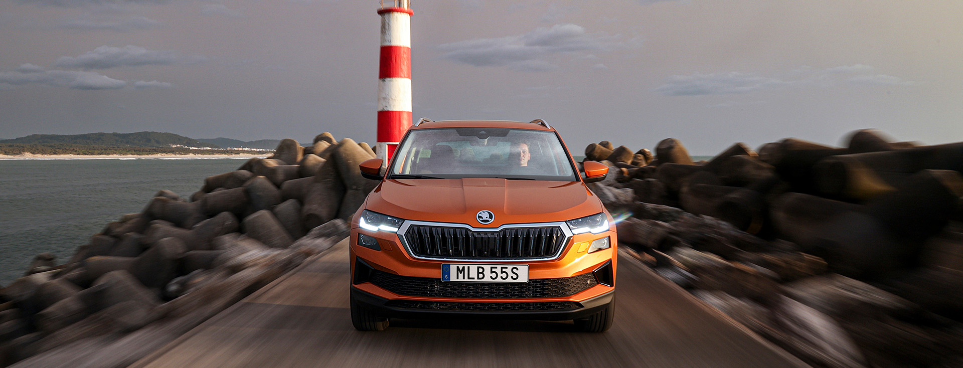 En orange Skoda Karoq ute på en pir med en fyr i bakgrunden