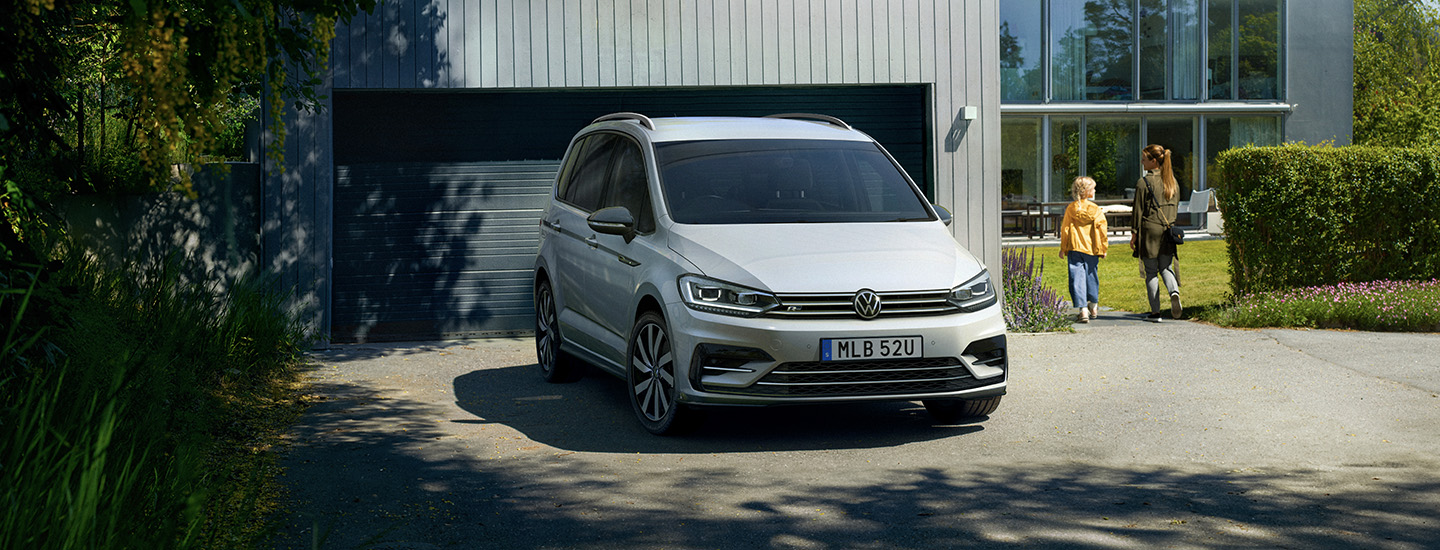 Touran parkerad framför garage, mamma och barn går mot huset
