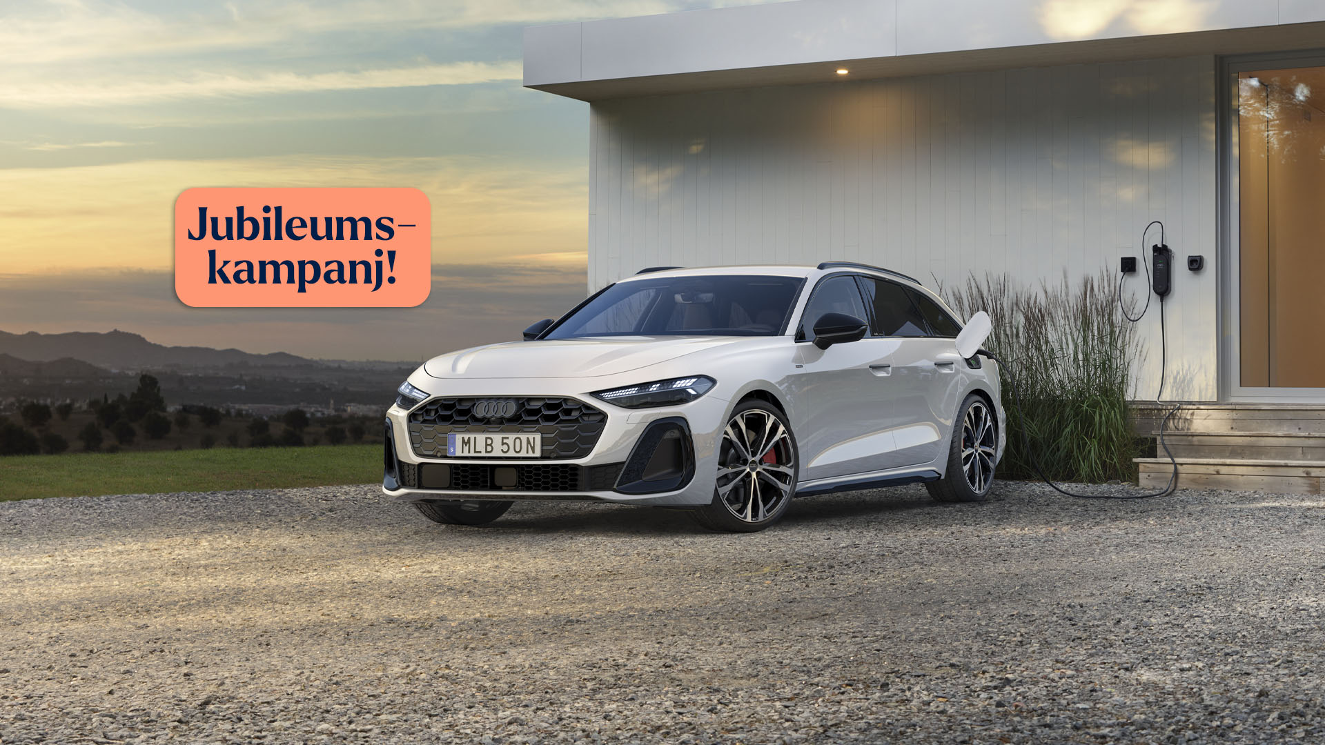 Vit Audi A5 framför villa,med laddsladd i.