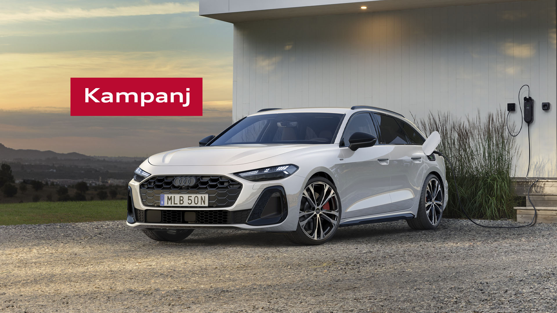 Audi A5 Avant e-hybrid står parkerad framför vitt putshus med laddaren ikopplad